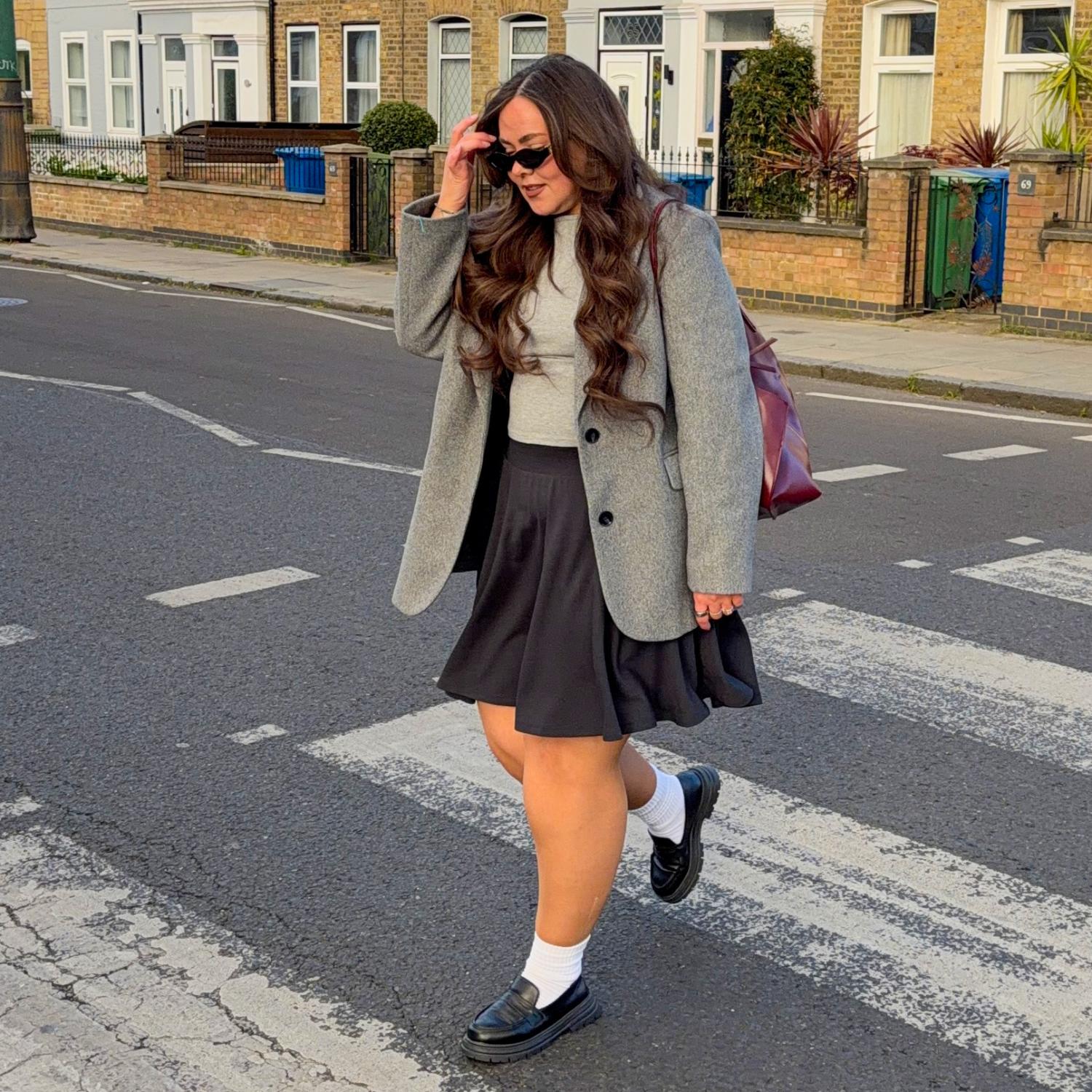 Woman walking on a street wearing a gray coat and charcoal skirt.