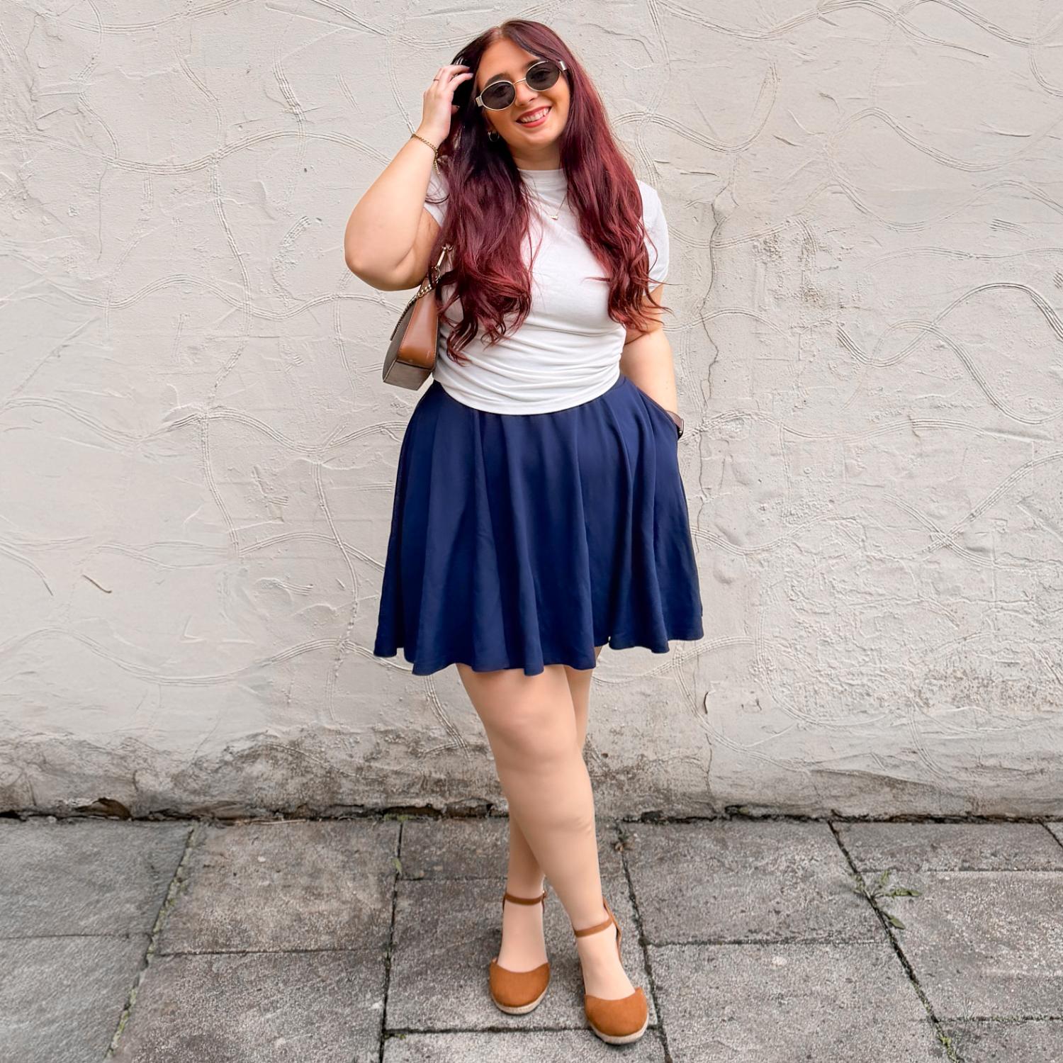 Woman wearing a white t-shirt and navy blue skirt against a textured wall.
